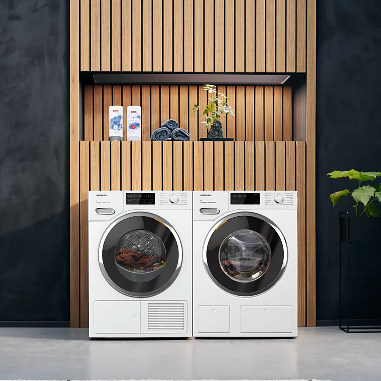A Miele washing machine and heat-pump dryer standing side by side on the floor in front of timber-slat joinery